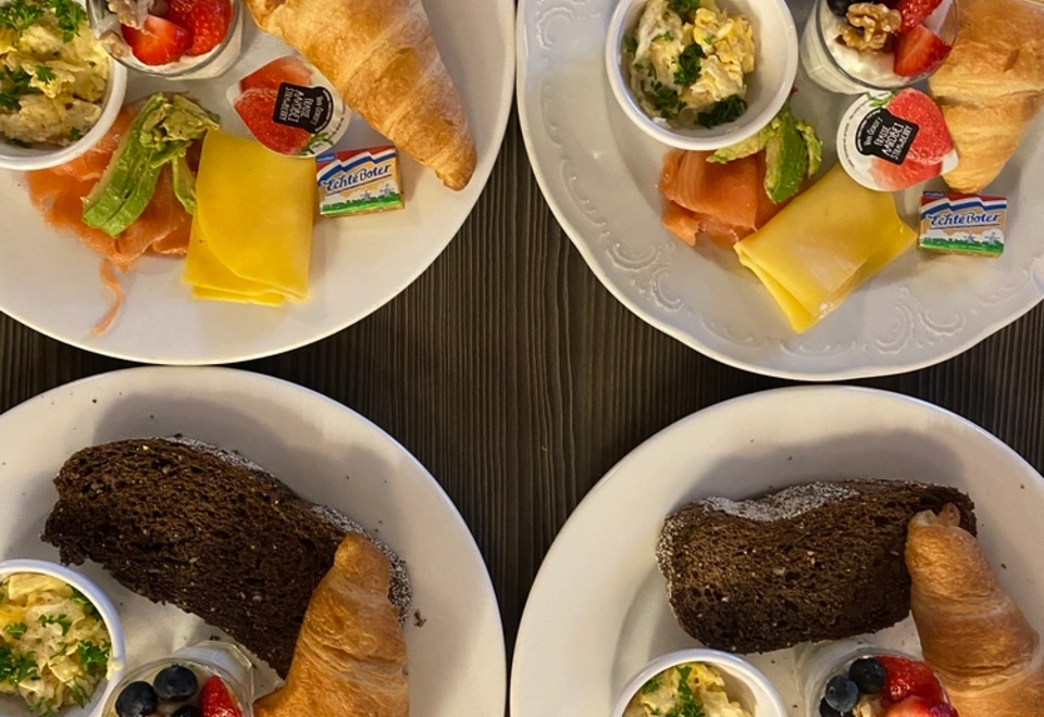 Frühstücksmenü mit Lachs oder italienischem Schinken, Joghurt mit Müsli, Croissant mit Käse und Rührei.
